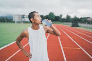 attraente asiatico sport uomo corridore stanco e assetato dopo in esecuzione allenarsi potabile acqua. sport uomo concetto. foto