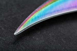 il curvo acuto lama di il kerambit pugnale è un' pendenza arcobaleno colore su un' buio sfondo. foto