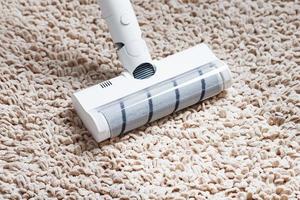 un' cordless vuoto addetto alle pulizie pulisce il tappeto nel il vivente camera con il parte inferiore di il gambe con un' pulito banda foto