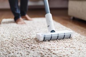 un' cordless vuoto addetto alle pulizie pulisce il tappeto nel il vivente camera con il parte inferiore di il gambe. moderno tecnologie per pulizia il Casa foto