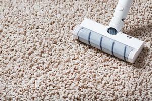 un' cordless vuoto addetto alle pulizie pulisce il tappeto nel il vivente camera con il parte inferiore di il gambe con un' pulito banda foto
