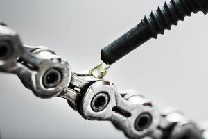 ingrassaggio un' bicicletta catena con un' far cadere di d'oro olio avvicinamento su un' grigio sfondo foto