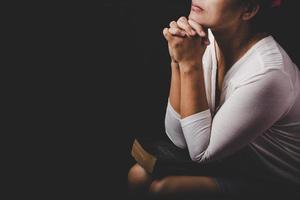 la mano della donna cristiana sulla Bibbia è pregare e adorare per ringraziare dio in chiesa con sfondo nero, concetto di fede, spiritualità e religione foto