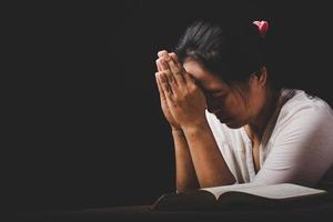 la mano della donna cristiana sulla Bibbia è pregare e adorare per ringraziare dio in chiesa con sfondo nero, concetto di fede, spiritualità e religione foto