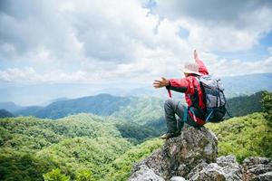 giovane escursionismo maschio sulla roccia in alto, zaino uomo che guarda la bellissima valle di montagna alla luce del sole in estate, paesaggio con uomo sportivo, alte colline, foresta, cielo. viaggi e turismo. foto