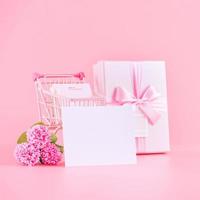 La madre di giorno vacanza regalo design concetto, rosa garofano fiore mazzo con avvolto scatola, shopping carrello, Borsa, isolato su leggero rosa sfondo, copia spazio. foto