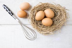 fresco biologico uova su nido con frusta su bianca di legno sfondo. foto