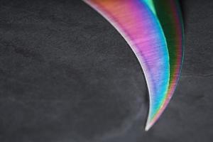 il curvo acuto lama di il kerambit pugnale è un' pendenza arcobaleno colore su un' buio sfondo. foto