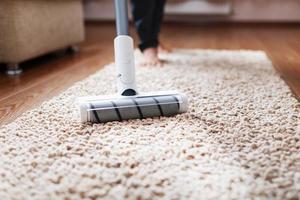 un' cordless vuoto addetto alle pulizie pulisce il tappeto nel il vivente camera con il parte inferiore di il gambe. foto