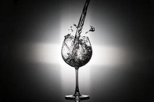 scrosciante acqua nel per il vino bicchiere con posteriore leggero su nero sfondo foto