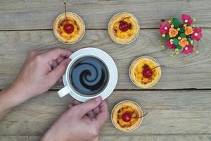 mano Tenere caffè tazza con uovo crostata su legna tavolo, piano Visualizza foto