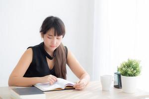 bella giovane donna asiatica sorridente seduta studio e apprendimento scrittura taccuino e diario in soggiorno a casa, compiti della ragazza, donna d'affari che lavora sul tavolo, concetto di istruzione. foto