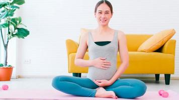 ritratto di bellissimo giovane asiatico incinta donna nel abbigliamento sportivo seduta su yoga stuoia a casa. foto