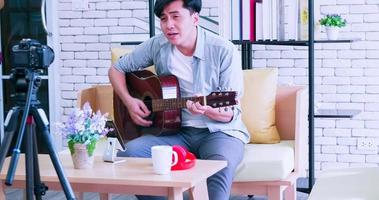 un' giovane asiatico uomo è giocando il chitarra e cantando su sociale media di streaming vivere a partire dal il suo casa. foto