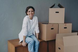 felice ragazza adolescente si muove. la signora ispanica è seduta sulle scatole nel nuovo appartamento e sorride. foto