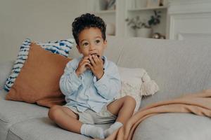 ragazzo afroamericano carino affamato che mangia cupcake mentre trascorre del tempo a casa foto