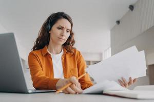 la giovane donna piuttosto europea esamina rapporti e grafici. il manager sta facendo brainstorming online da casa. foto