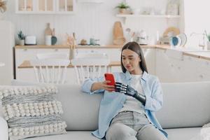 la donna disabile sta scrivendo sullo smartphone. ragazza felice che tiene il telefono con il braccio artificiale bionico. foto