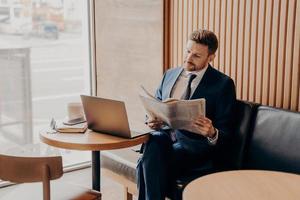 concentrato ricco uomo d'affari che legge il giornale nella caffetteria foto