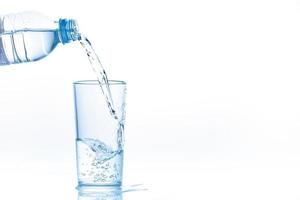 scrosciante acqua a partire dal bottiglia in bicchiere su bianca sfondo. foto con copia spazio.