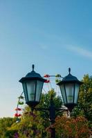 paesaggio di un parco divertimenti con lanterna decorata con fiori sullo sfondo la parte superiore di una ruota panoramica che mostra sopra le cime degli alberi contro un cielo blu. foto