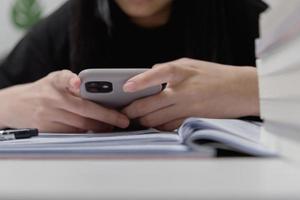 asiatico giovane ragazza uso un' mobile inteligente Telefono per studia formazione scolastica in linea a casa. foto