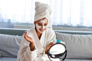 terme a casa. donna a casa è l'applicazione facciale foglio maschera. cosmetico procedure, maschera per pelle cura, donna giovane, terme salone. bellissimo donna con terme facciale maschera. foto