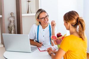 ritratto di giovane sorridente femmina dietologo nel il consultazione camera. fabbricazione dieta Piano. giovane donna visitare dietologo nel peso perdita clinica foto