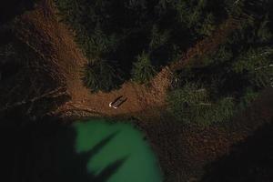 aereo Visualizza di Due persone in piedi di il naturale lago circondato di pino alberi nel karpaty montagne, Ucraina. alto qualità foto