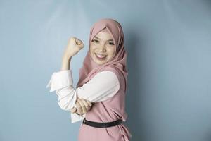 eccitato asiatico musulmano donna indossare un' rosa hijab mostrando forte gesto di sollevamento sua braccia e muscoli sorridente con orgoglio foto