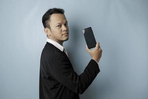 un' giovane asiatico uomo d'affari nel un' nero completo da uomo si sente grave e messa a fuoco Tenere un' smartphone e mostrando il copia spazio su suo schermo nel mano. foto