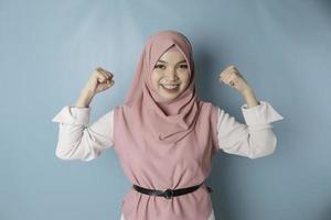 eccitato asiatico musulmano donna indossare un' rosa hijab mostrando forte gesto di sollevamento sua braccia e muscoli sorridente con orgoglio foto