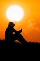 silhouette di un disoccupato uomo seduta e Guardando Telefono per trova opera foto