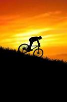 un' silhouette di un' ciclista discendente a partire dal il montagna nel il sera. foto