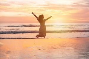 giovane donna salto su il spiaggia a bellissimo tramonto, estate vacanza concetto foto