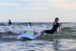 giovane poco asiatico ragazzo surfer caduta a partire dal tavola in mare onda con contento e divertente viso. foto