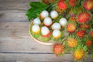 rambutan frutta raccogliere a partire dal il giardino rambutan albero, fresco e maturo rambutan dolce tropicale frutta pelato rambutan con foglia su di legno piatto foto