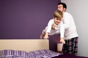 contento uomo giocando con il suo figlio nel il Camera da letto. foto