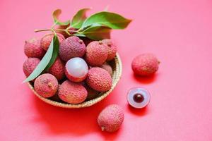 lychee fetta pelato su rosso rosa sfondo - fresco lychee con verde le foglie raccogliere nel cestino a partire dal albero tropicale frutta estate nel Tailandia foto