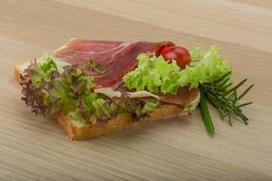 prosciutto Sandwich su di legno tavola e bianca sfondo foto