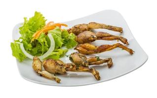 grigliato rana gambe su il piatto e bianca sfondo foto