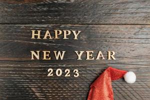 contento nuovo anno 2023 saluto carta. citazione fatto di di legno lettere su di legno sfondo con rosso Santa cappello. festivo sfondo foto