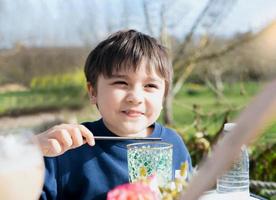 ritratto giovane ragazzo potabile fresco succo per prima colazione nel bar, contento bambino ragazzo potabile bicchiere di bibita o morbido freddo bevanda mentre in attesa per cibo nel ristorante nel il soleggiato giorno mattina foto