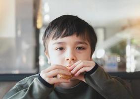 ritratto ragazzo mordere hash Marrone per colazione, salutare bambino ragazzo mangiare inglese prima colazione nel il bar o ristorante, salutare cibo concetto foto