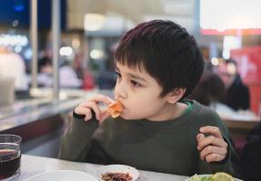 sano giovane ragazzo mangiare salmone sashimi nel giapponese buffet ristorante , ragazzo utilizzando bastoncini avendo giapponese cibo per pranzo nel il bar foto