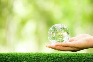 umano mano Tenere globo pianeta bicchiere nel verde foresta con bokeh natura luci. mondo ambiente giorno. concetto per ambiente conservazione, proteggere ecologia terra e ambientale eco-friendly vita. foto