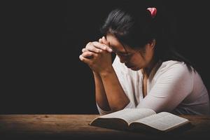 la mano della donna cristiana sulla Bibbia è pregare e adorare per ringraziare dio in chiesa con sfondo nero, concetto di fede, spiritualità e religione foto