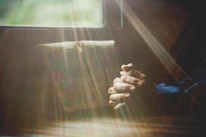 mano piegato nel preghiera per Dio su santo Bibbia libro nel Chiesa concetto per fede, spiritualità e religione, donna persona preghiere su santo Bibbia nel mattina. cristiano cattolico donna mano con Bibbia culto. foto