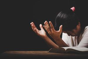 la mano della donna cristiana sulla Bibbia è pregare e adorare per ringraziare dio in chiesa con sfondo nero, concetto di fede, spiritualità e religione foto