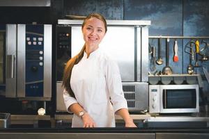 ritratto di fiducioso e sorridente giovane donna capocuoco vestito nel bianca uniforme, professionale cucina siamo su sfondo foto